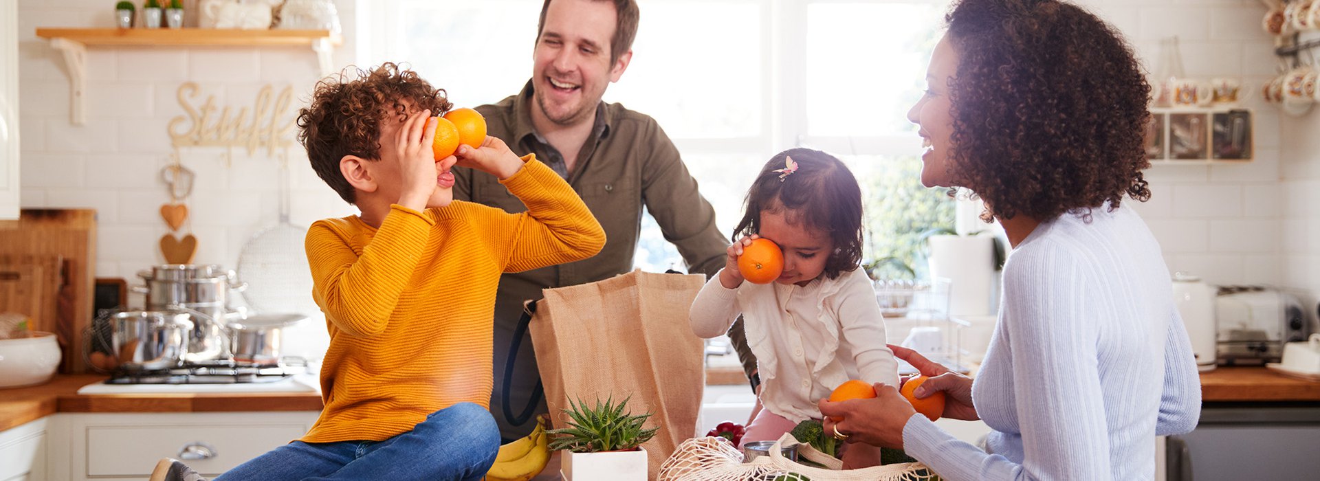 Family Returning Home From Shopping Trip Using Plastic Free Bags Unpacking Groceries In Kitchen